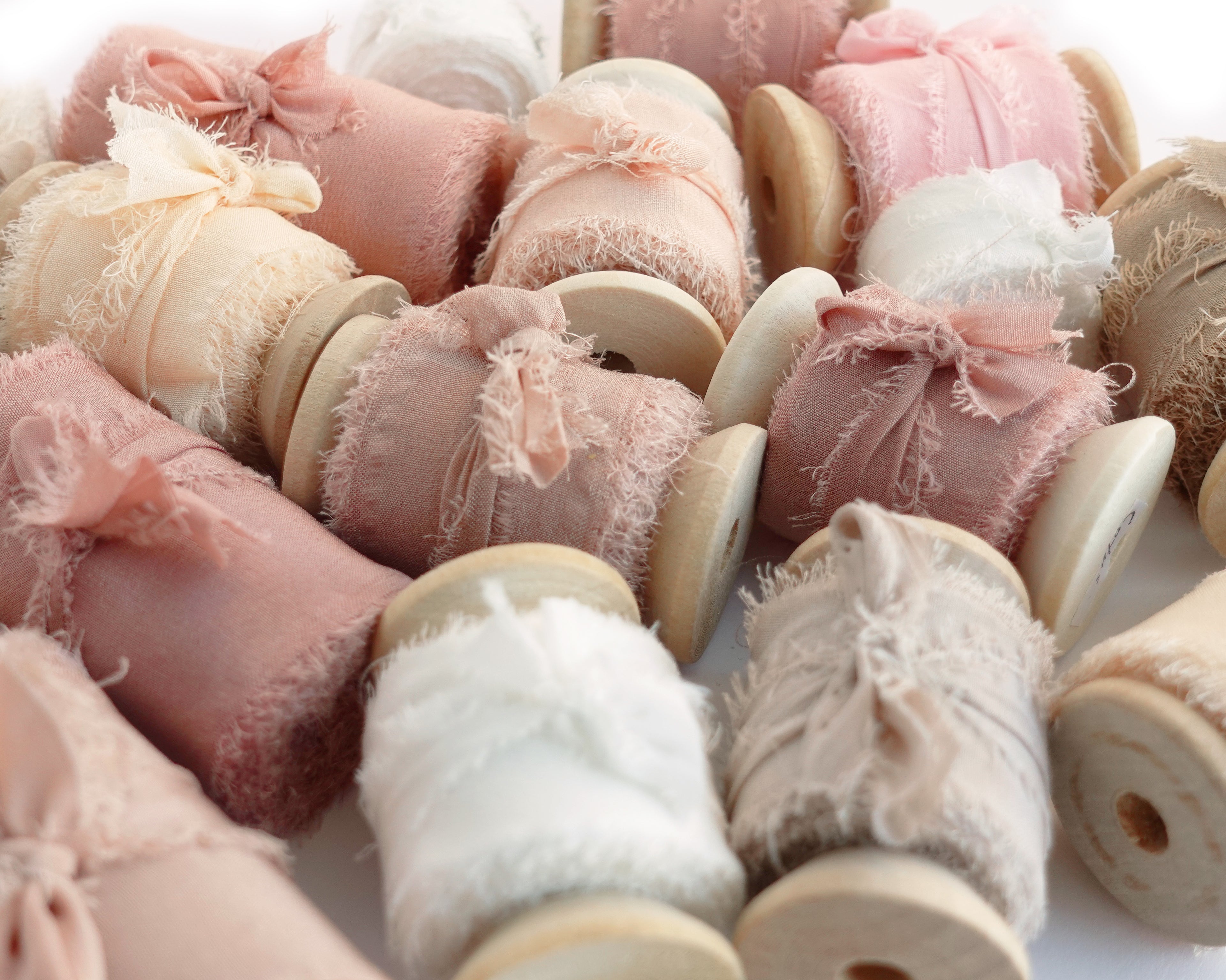 Pink beige and white ribbons rolled on wooden spools closed with bows